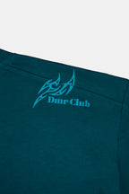 Detalle de estampado DTF a la altura del hombro en polo boxy fit manga corta para hombre en color verde esmeralda. 